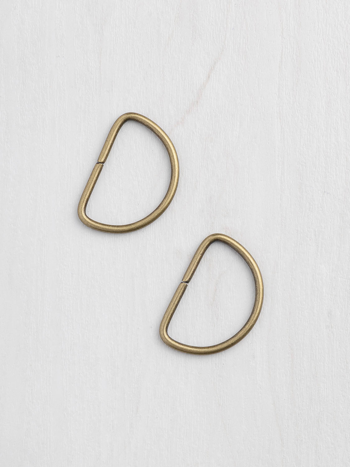 Two brass D-shaped hooks on a white background