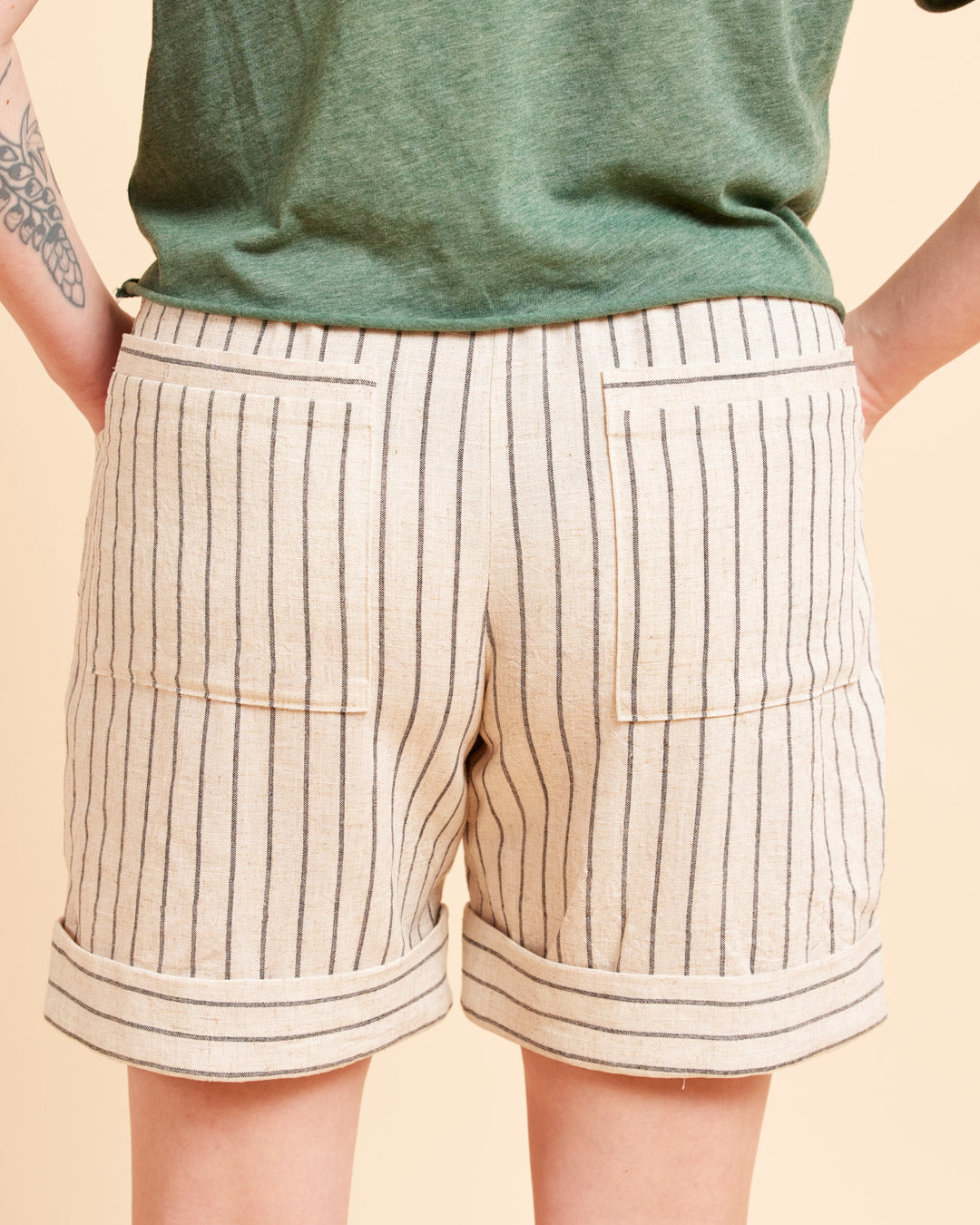 Beige shorts with black stripes worn by a person on a beige background. These shorts are the Everett Pants & Shorts sewing pattern from Cashmerette.