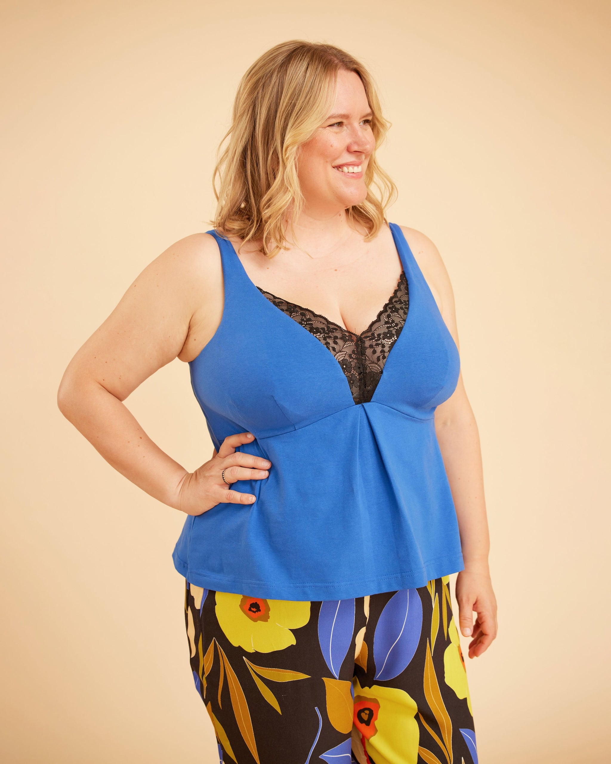 Woman wearing a blue top with floral pants on a beige background. This is the Fiske Sleepwear Set sewing pattern from Cashmerette.